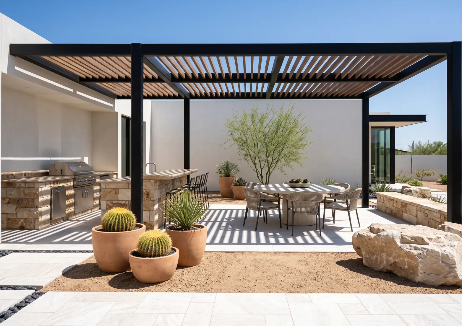 Modern desert patio with a slatted pergola, a stone outdoor kitchen and a round dining table in midday sun